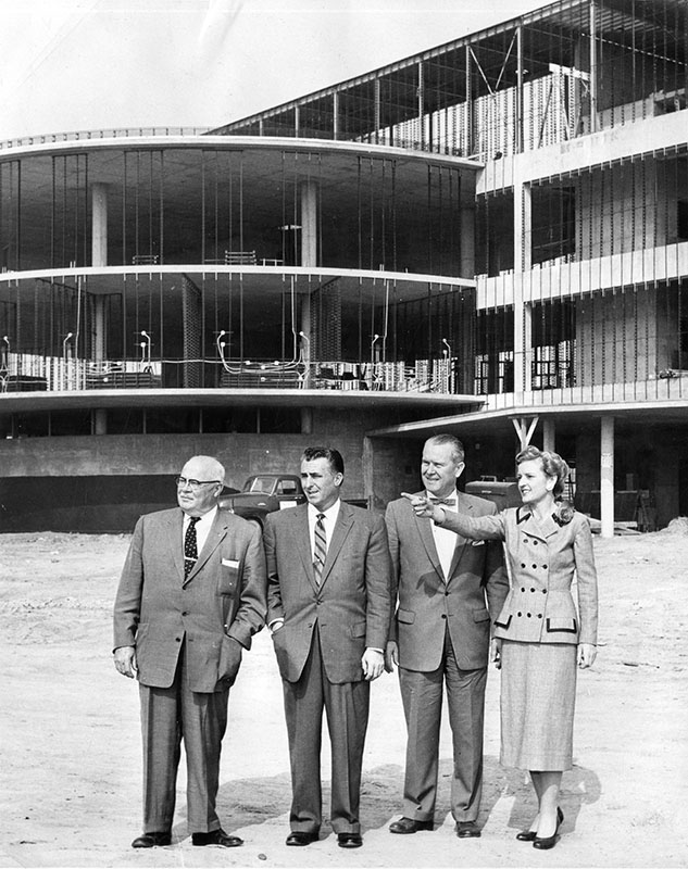 March 18, 1957 reads "Discussing modern innovations of Valley Presbyterian Hospital, nearing completion at 15107 Vanowen St., are Mrs. Barbara Holt, member of hospital's board of directors, and from left, J. H. Wray, Jim Cross and Walter Rueff, members of San Fernando Automobile Dealers Association committee for hospital's fund drive."  (LAPL)