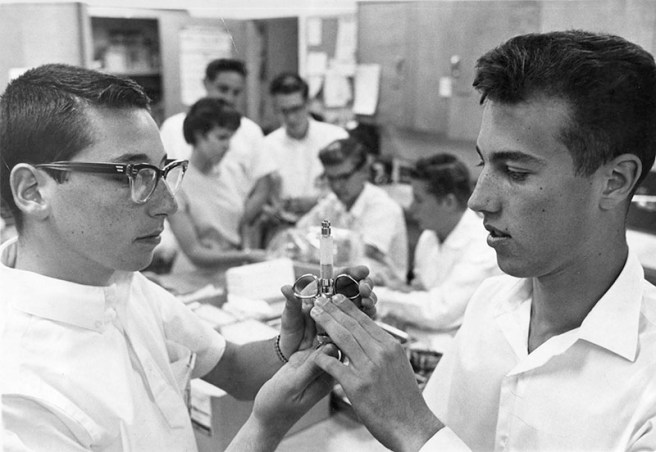 Photograph caption dated February 20, 1961 reads "Larry Peskin, 17, left, 10038 Noble St., Sepulveda, completes hospital course. Fellow graduate examining syringe is Warren Wilkinson, 17, 9439 Louise Ave., Northridge." The young men completed a 20-hour training course to become volunteers at Valley Presbyterian Hospital in Van Nuys. Ph: Jon Woods