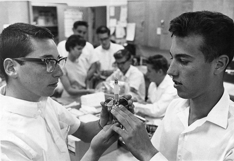 Photograph caption dated February 20, 1961 reads "Larry Peskin, 17, left, 10038 Noble St., Sepulveda, completes hospital course. Fellow graduate examining syringe is Warren Wilkinson, 17, 9439 Louise Ave., Northridge." The young men completed a 20-hour training course to become volunteers at Valley Presbyterian Hospital in Van Nuys. Ph: Jon Woods